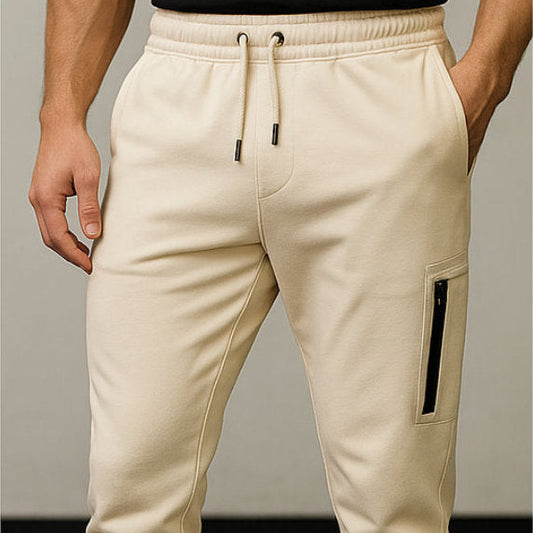 Beige jogger pants with a black patch on a neutral background