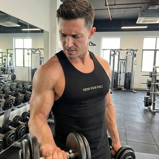 Man lifting weights in a gym wearing a black tank top with visible branding.